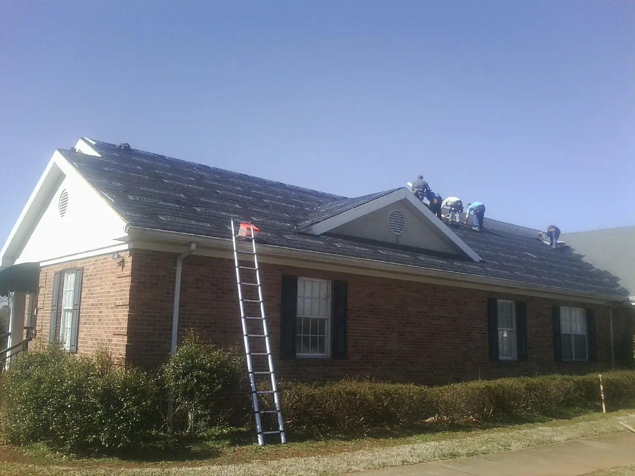 Crew tearing shingles off a brick ranch roof with a ladder set — Metal Roof Repair work by our crew in Panama City Beach