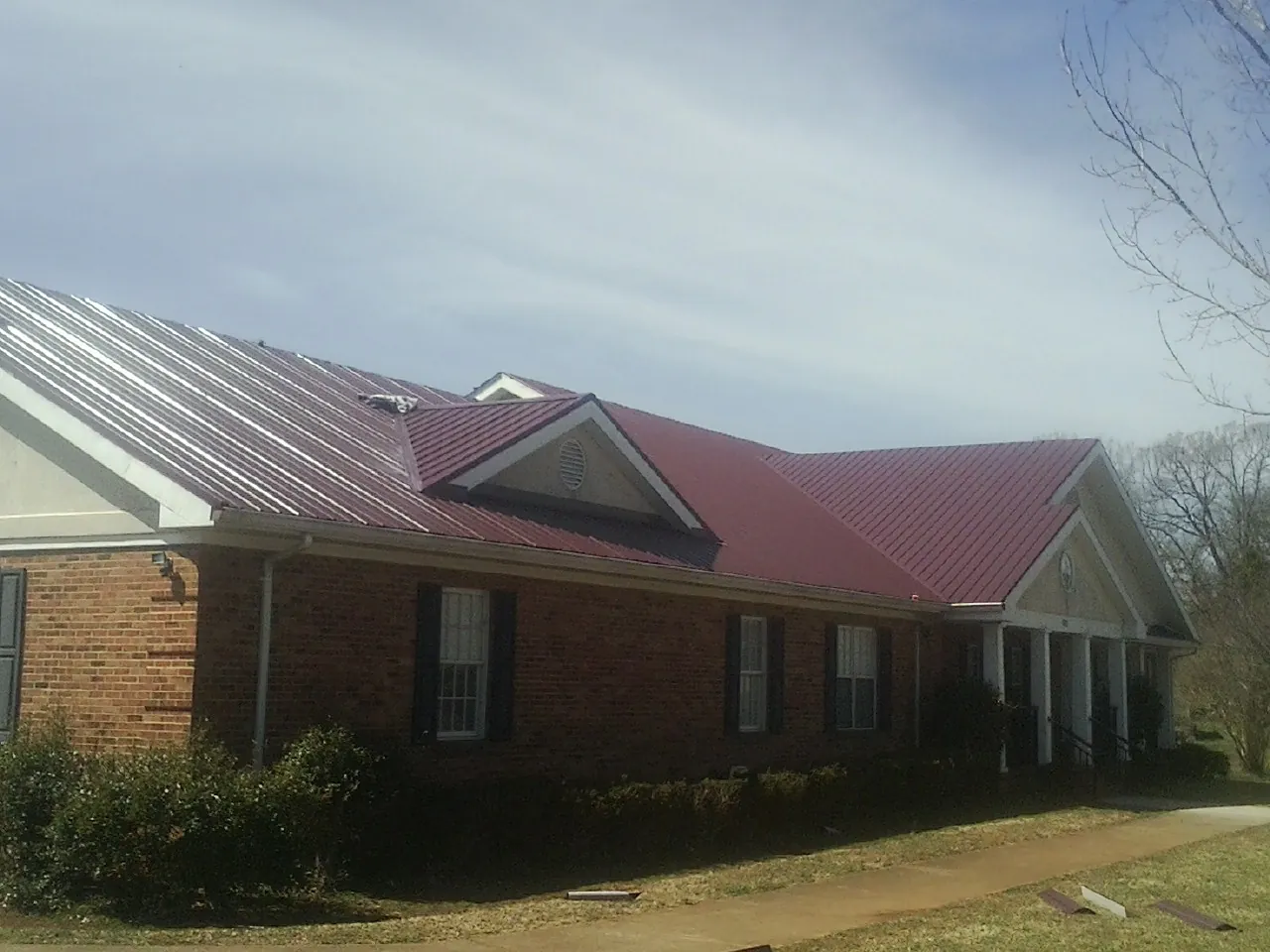 Red metal roof with gabled entries on a long brick building, from a Hail Damage Roof Repair job in Panama City Beach