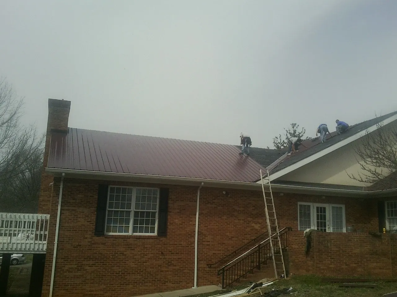 Crew setting red metal roofing panels on a brick home in Panama City Beach