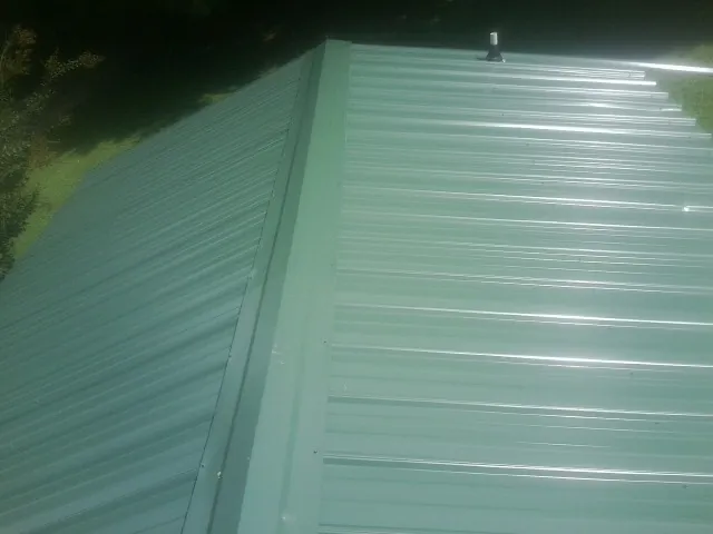 New green metal panels meeting at the ridge of a roof — Flat Roof Repair work by our crew in Panama City Beach