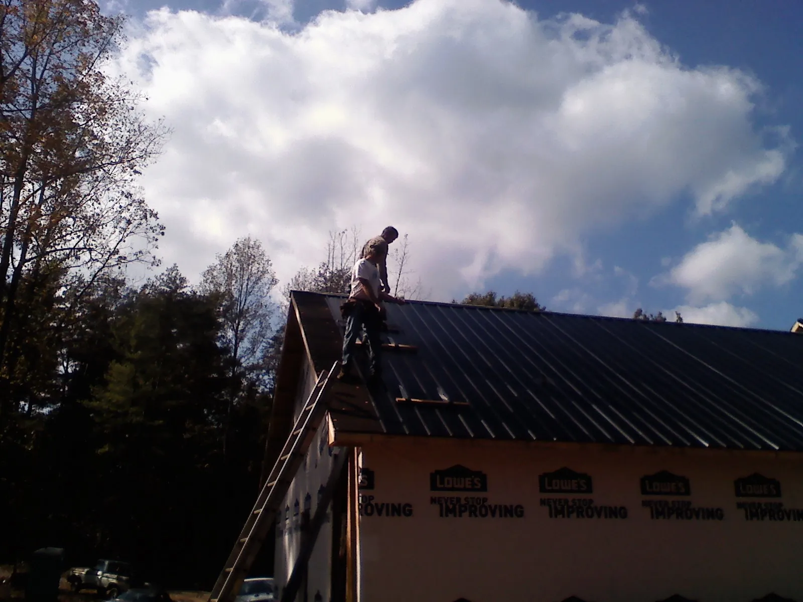 Roofer fastening dark metal panels high against a cloudy sky, from a Roof Inspection job in Panama City Beach