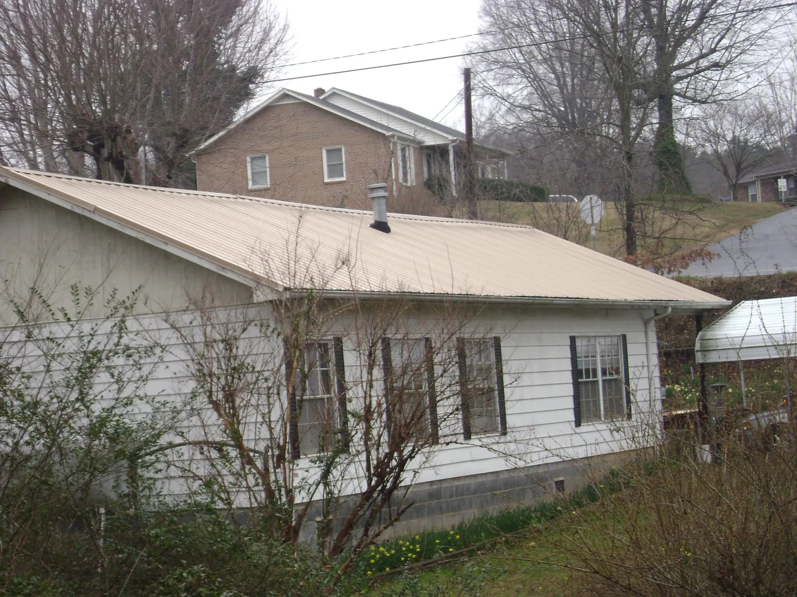 Tan metal roof on a white sided house set into a hillside — Commercial Roofing by Roofing Brothers in Panama City Beach