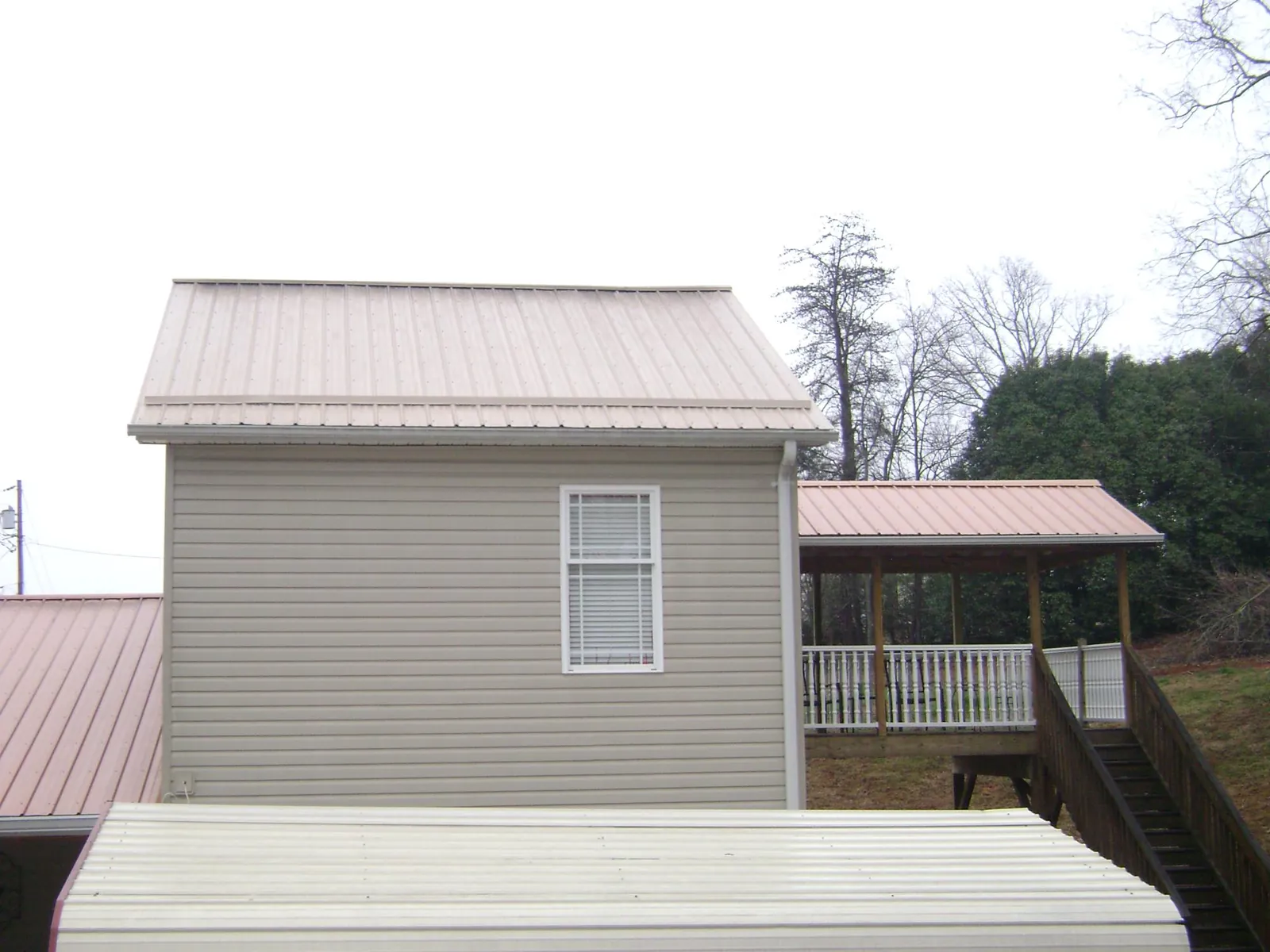 Tan metal roofs on a two story addition and attached porch, from a Roof Replacement job in Panama City Beach